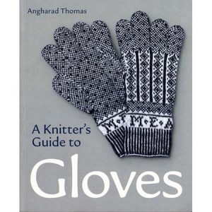 cover for the book A Knitter's Guide to Gloves by Angharad Thomas. A pair of blue and white gloves pictured large on a gray cover. Gloves have blue diamond -like shape patterns and lines with fingers in tweedy blue and white. Initials above the cuff MEA i