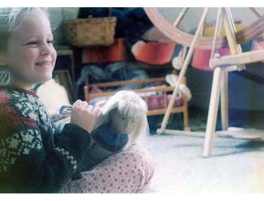 Young blonde girl playing with blonde doll, spinning wheel and craft items in background