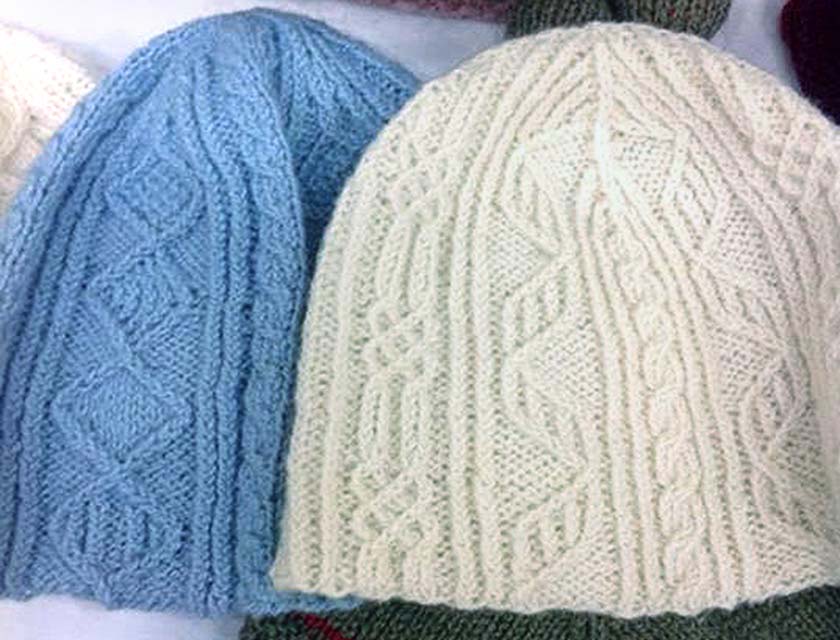close up showing one cream and one blue twisted stitch hats