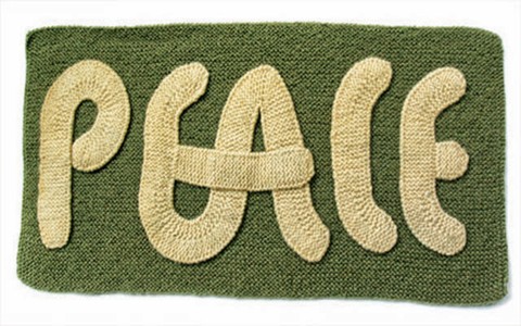 knitted word peace in cream script on green background