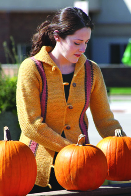 young woman wearing a yellow and pink striped suspender cardigan looking at pumpkins