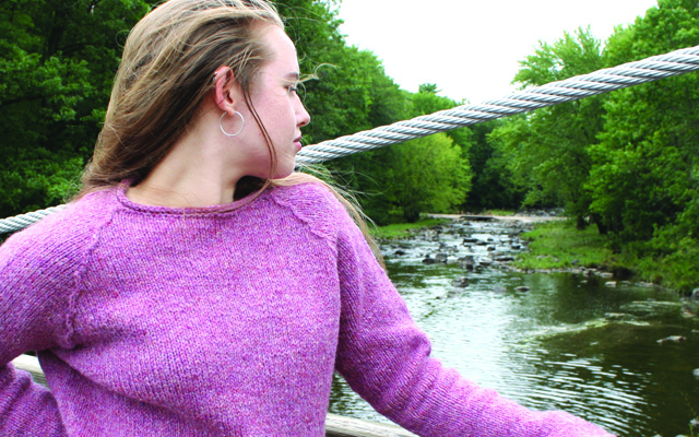 woman in pink sweater on suspension bridge over river